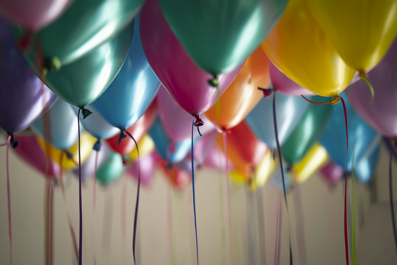 Cluster of colorful helium balloons against a pale wall