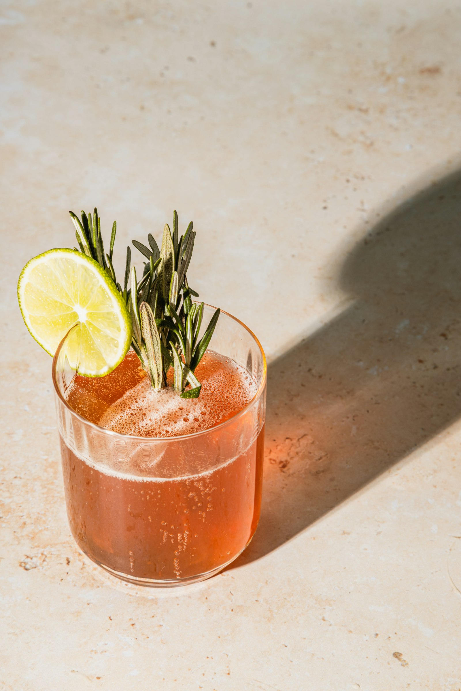Pale pink cocktail with rosemary and a lime wheel