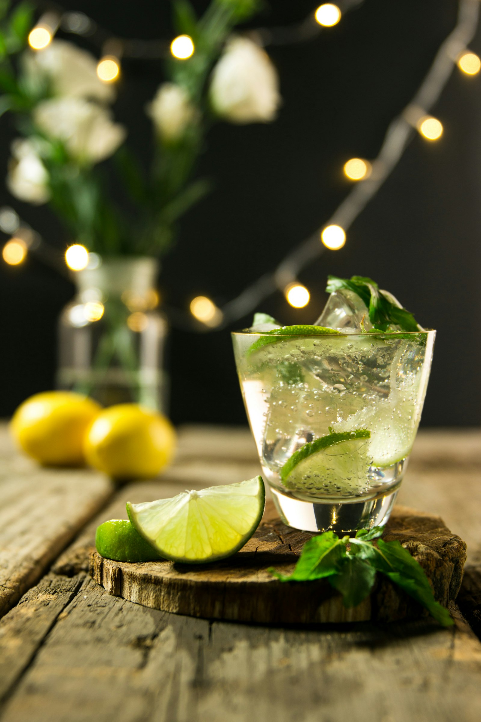 Clear lime cocktail on a wood round with mint and string lights