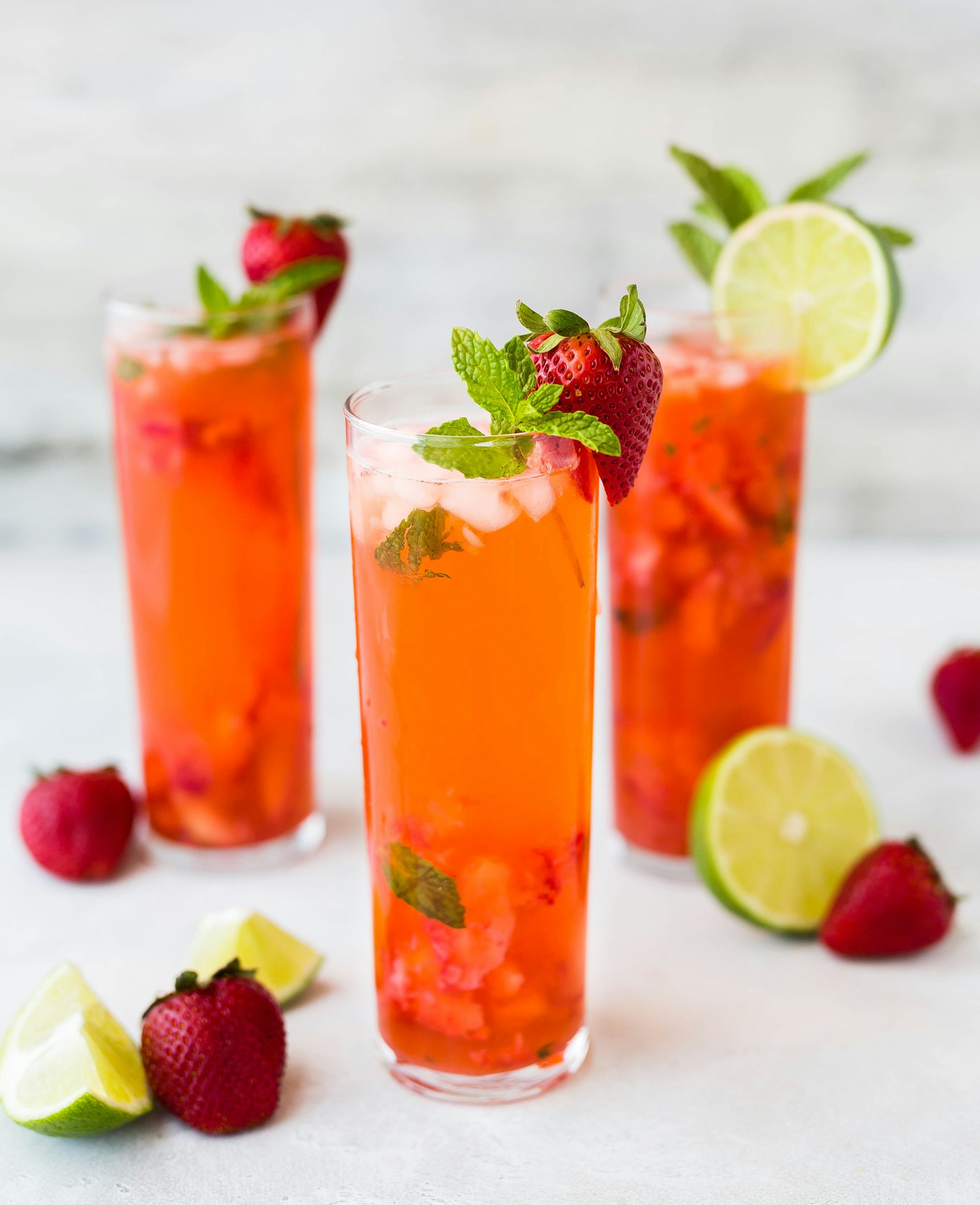 Three tall strawberry cocktails garnished with mint and lime