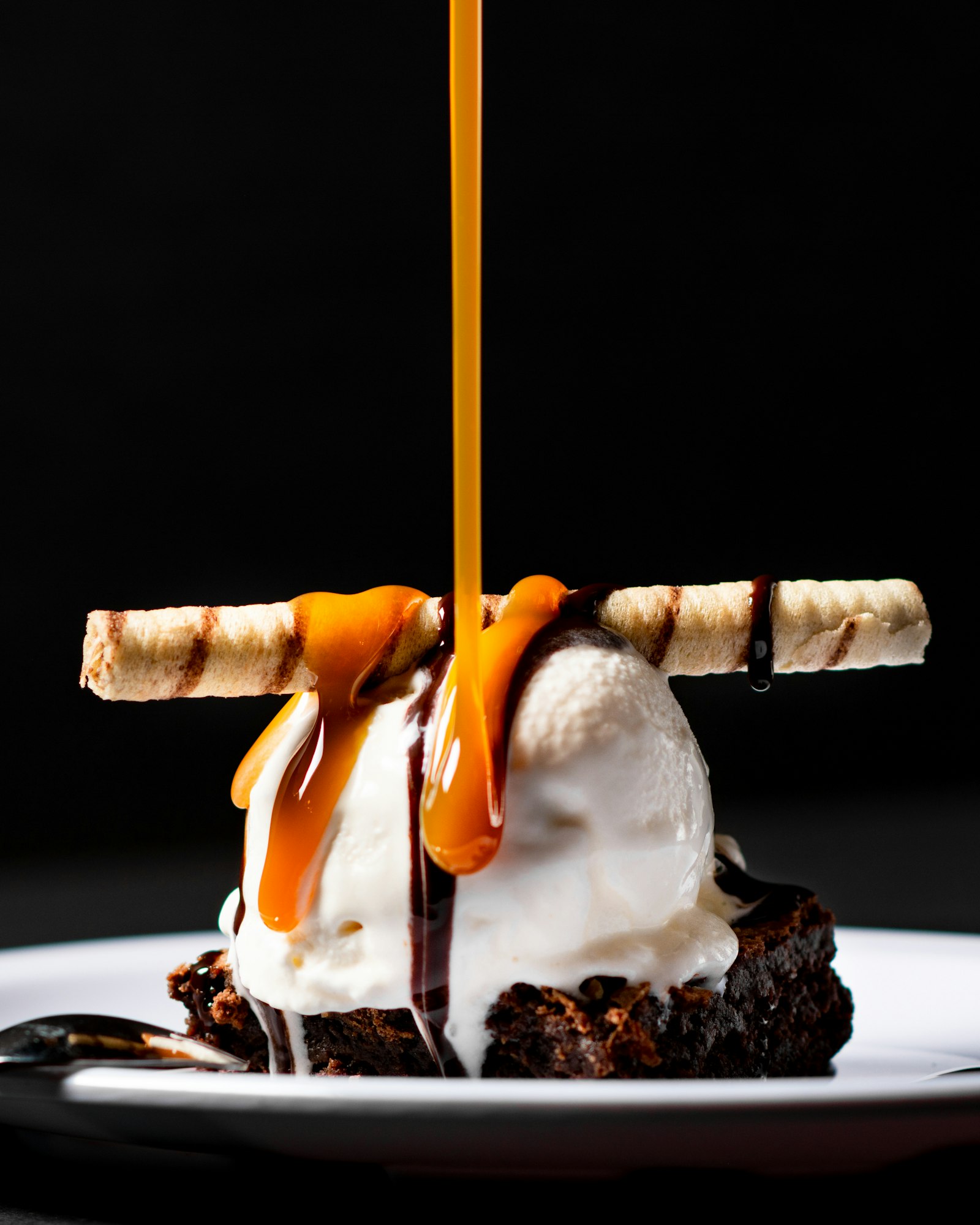 Brownie sundae with ice cream, a wafer stick, and a caramel pour