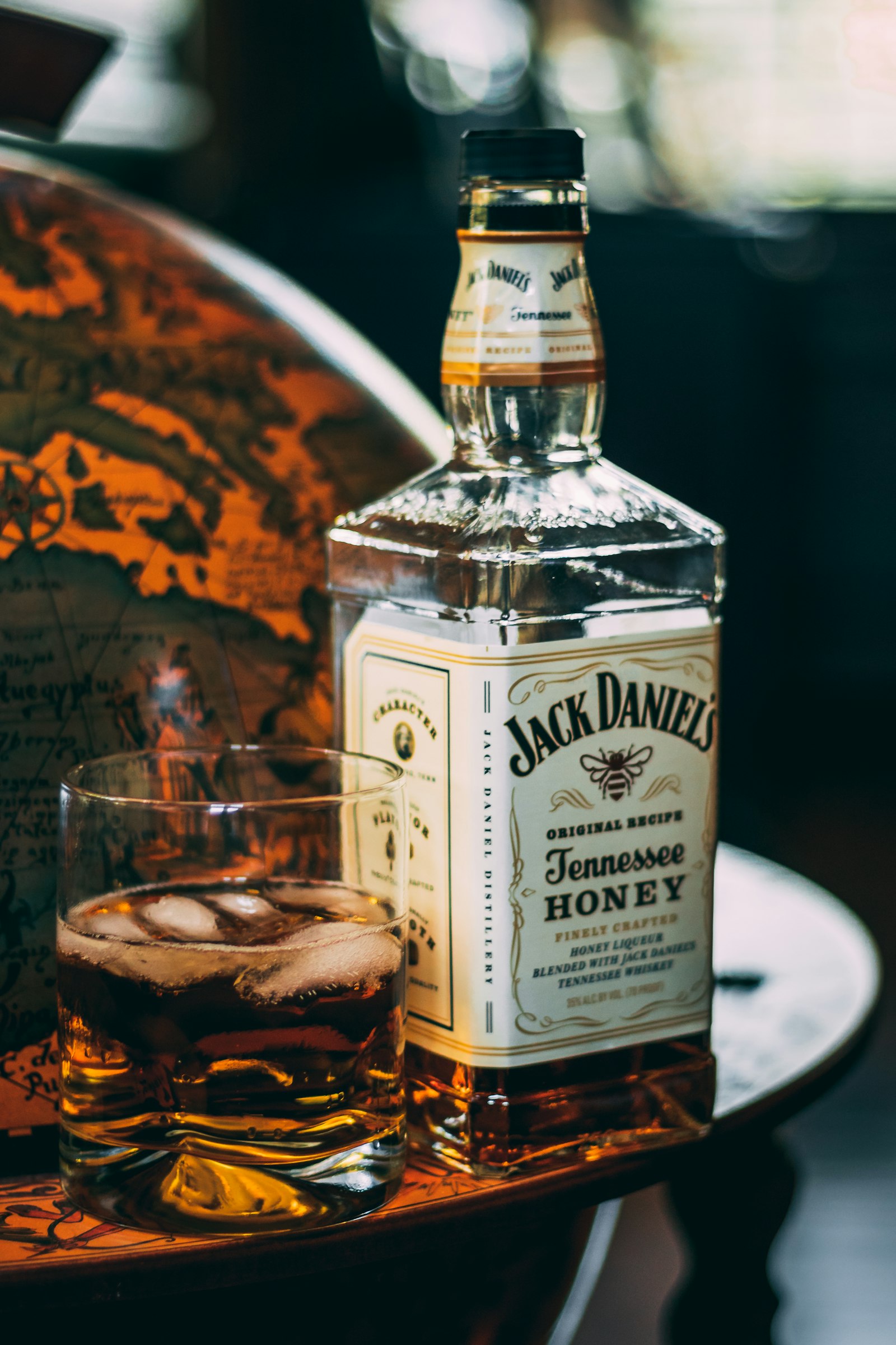 Rocks glass of whiskey beside a honey whiskey bottle